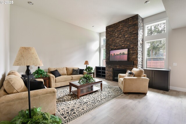 living room with plenty of natural light, a stone fireplace, and light wood-type flooring