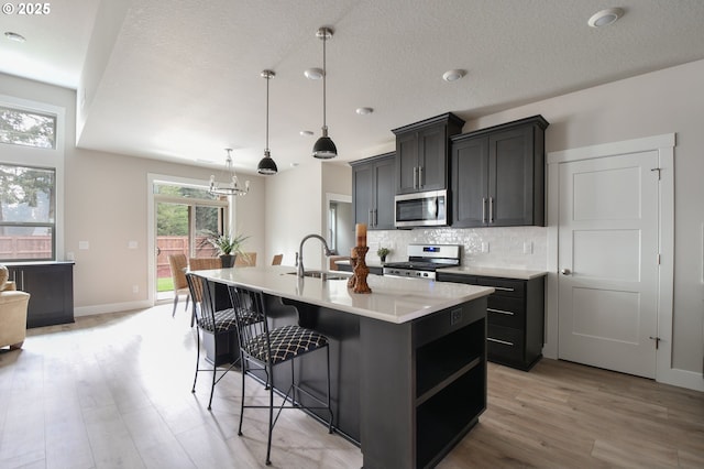 kitchen featuring hanging light fixtures, gas range, sink, backsplash, and a center island with sink