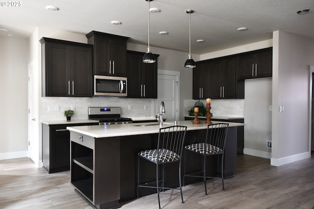 kitchen featuring sink, light hardwood / wood-style flooring, appliances with stainless steel finishes, a center island with sink, and decorative light fixtures