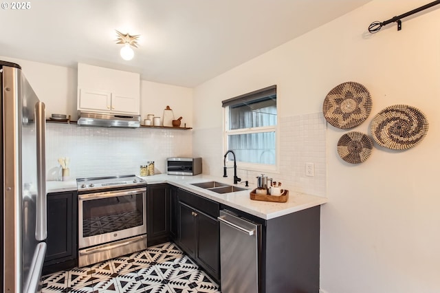 kitchen with a sink, under cabinet range hood, stainless steel appliances, light countertops, and decorative backsplash