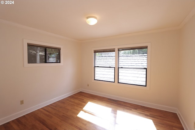 empty room featuring visible vents, crown molding, baseboards, and wood finished floors