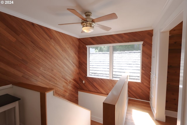 interior space with ornamental molding, wood walls, a ceiling fan, and baseboards