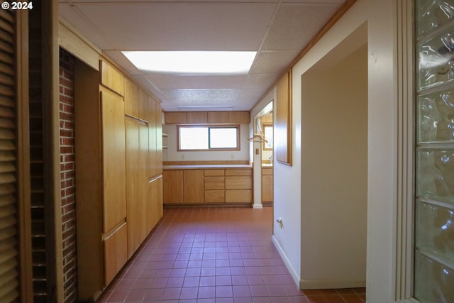 hall with dark tile patterned floors, baseboards, and a drop ceiling