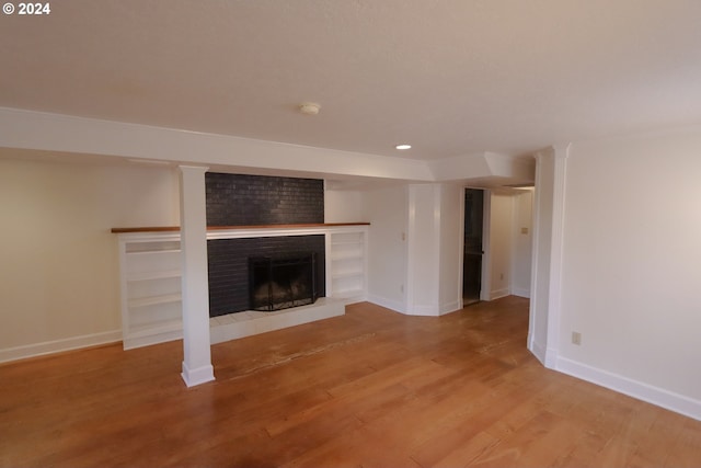 unfurnished living room featuring light wood-type flooring, a brick fireplace, and baseboards