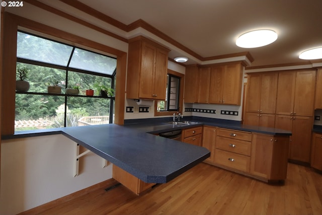 kitchen featuring brown cabinetry, dark countertops, light wood-style flooring, a kitchen breakfast bar, and a peninsula