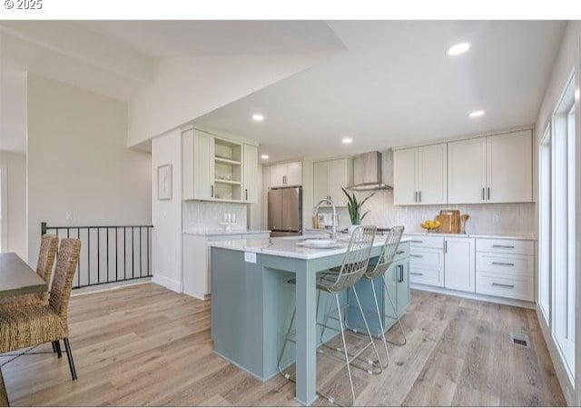 kitchen featuring open shelves, a sink, wall chimney range hood, freestanding refrigerator, and light countertops