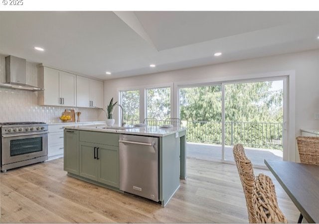 kitchen with light wood-style flooring, stainless steel appliances, wall chimney exhaust hood, and light countertops