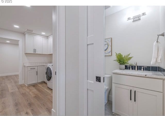 washroom featuring light wood-style flooring, washer / clothes dryer, cabinet space, recessed lighting, and a sink