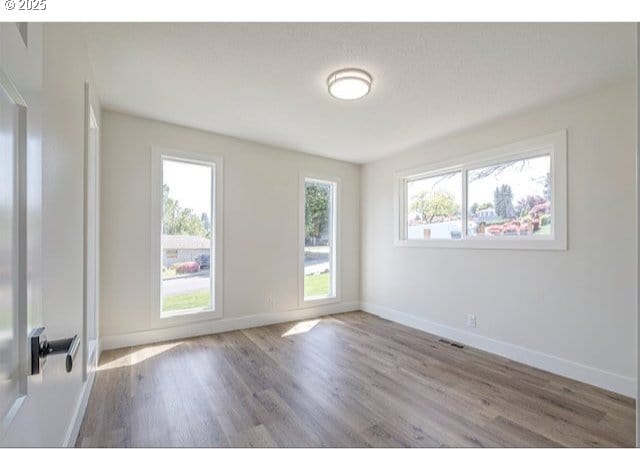 unfurnished room with a wealth of natural light, baseboards, and wood finished floors