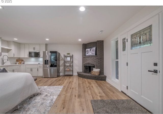 bedroom with a fireplace, recessed lighting, stainless steel fridge with ice dispenser, a sink, and light wood-style floors