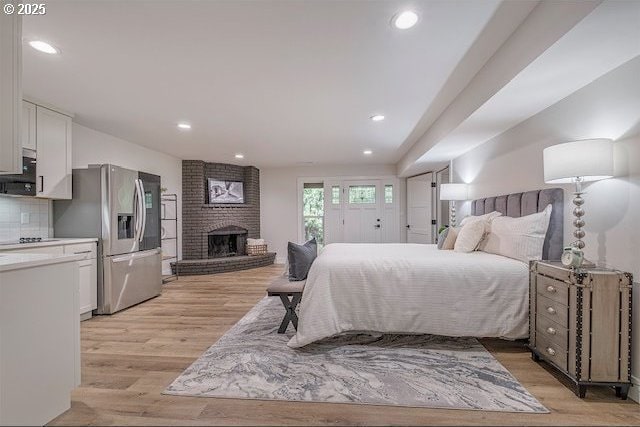 bedroom with recessed lighting, a brick fireplace, light wood-style floors, and stainless steel fridge with ice dispenser