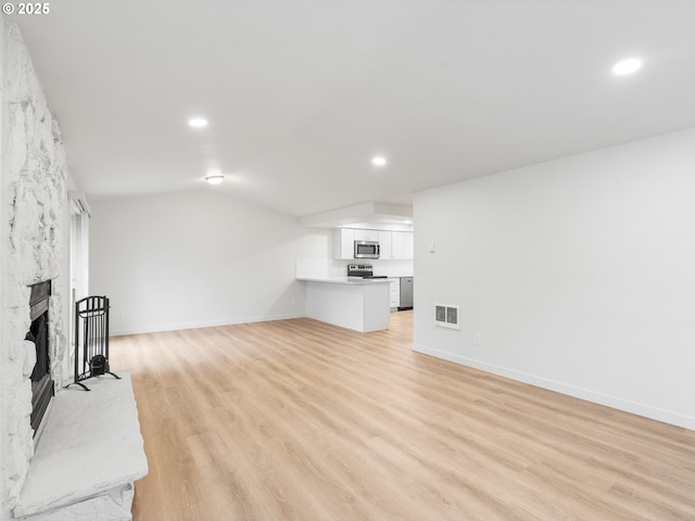 living room featuring lofted ceiling, a fireplace, and light wood-type flooring