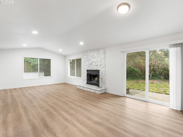 unfurnished living room with light hardwood / wood-style floors, vaulted ceiling, and a stone fireplace