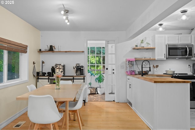 kitchen featuring open shelves, appliances with stainless steel finishes, plenty of natural light, and butcher block counters