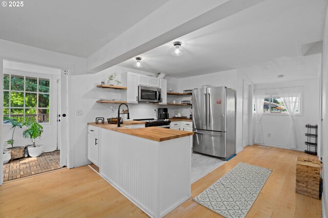 kitchen with stainless steel appliances, open shelves, butcher block countertops, and a healthy amount of sunlight