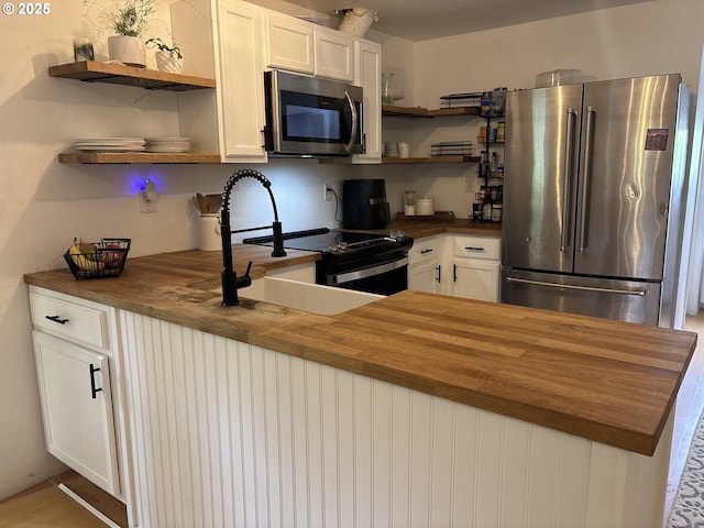 kitchen featuring white cabinets, open shelves, appliances with stainless steel finishes, a sink, and wood counters