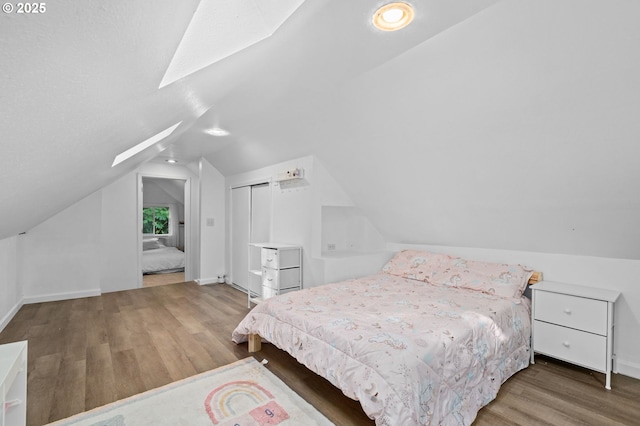 bedroom featuring baseboards, lofted ceiling with skylight, and wood finished floors