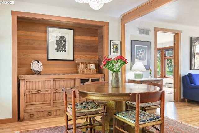 dining room with a baseboard heating unit, wood walls, wood finished floors, and visible vents