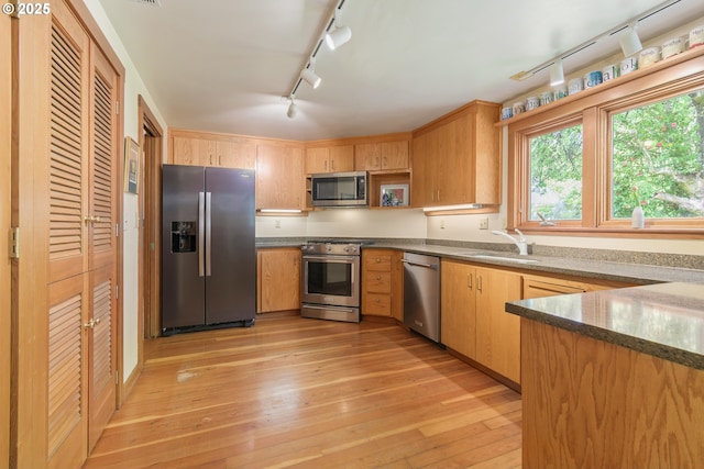 kitchen featuring a sink, stainless steel appliances, rail lighting, and light wood-style flooring