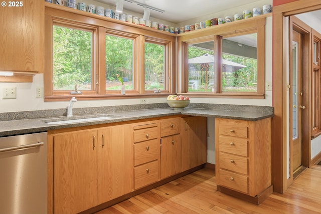 kitchen with stainless steel dishwasher, dark countertops, a sink, and light wood-style floors
