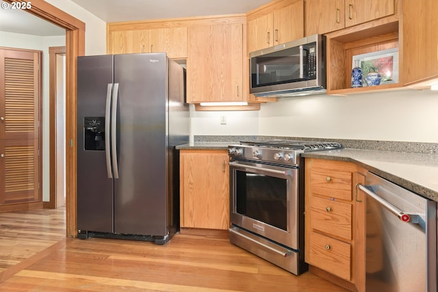 kitchen with light brown cabinetry, dark countertops, appliances with stainless steel finishes, and light wood finished floors