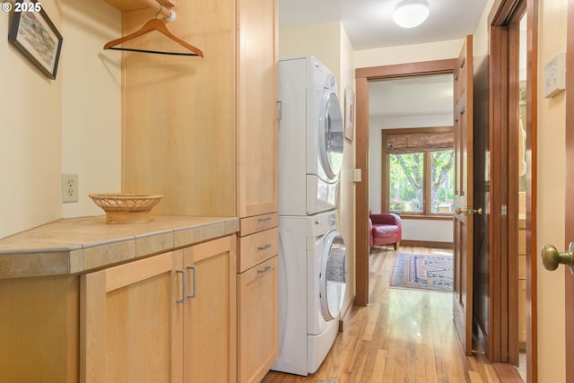 clothes washing area featuring light wood-type flooring, cabinet space, and stacked washer / dryer