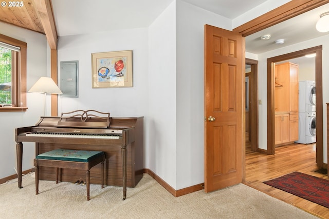 sitting room featuring beamed ceiling, baseboards, light colored carpet, electric panel, and stacked washer / drying machine