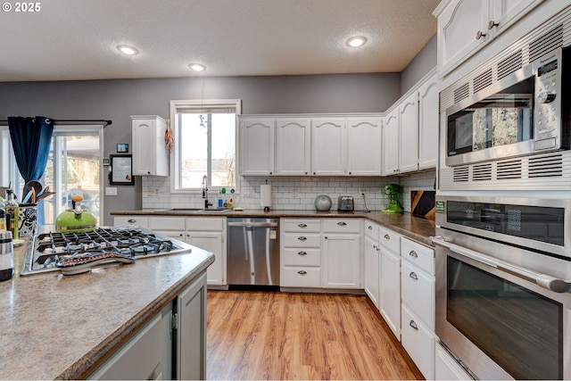 kitchen featuring appliances with stainless steel finishes, sink, white cabinets, decorative backsplash, and light hardwood / wood-style flooring