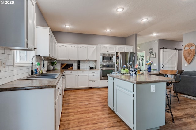 kitchen featuring sink, a breakfast bar, appliances with stainless steel finishes, white cabinets, and a barn door