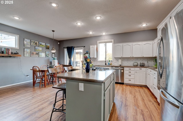 kitchen with a kitchen island, white cabinetry, hanging light fixtures, stainless steel appliances, and light wood-type flooring