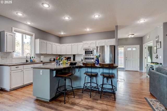 kitchen with a breakfast bar area, white cabinetry, a kitchen island, stainless steel appliances, and light hardwood / wood-style floors