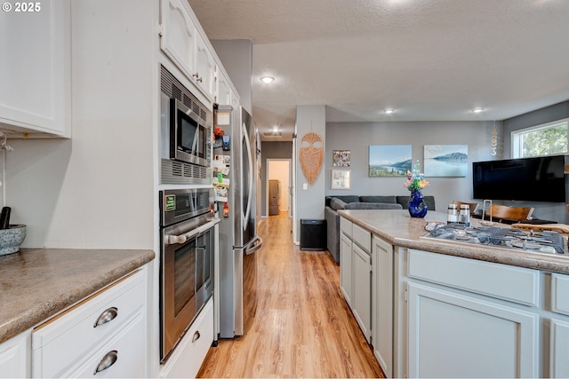 kitchen with a textured ceiling, stainless steel appliances, light hardwood / wood-style floors, and white cabinets