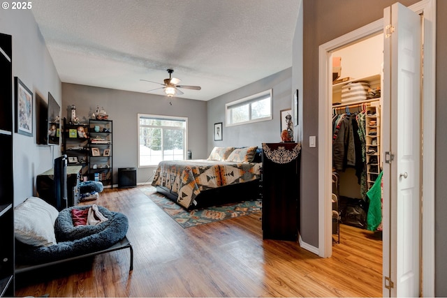 bedroom featuring light wood-type flooring, a spacious closet, ceiling fan, a textured ceiling, and a closet