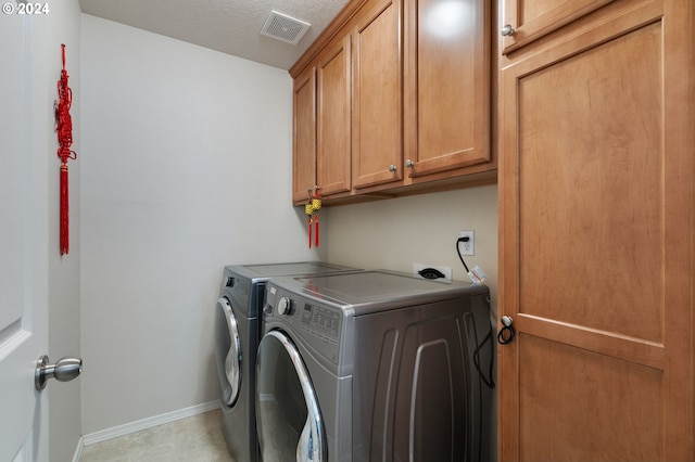 laundry room with cabinets, washing machine and clothes dryer, and a textured ceiling