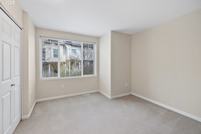 unfurnished bedroom featuring a closet, light carpet, baseboards, and visible vents