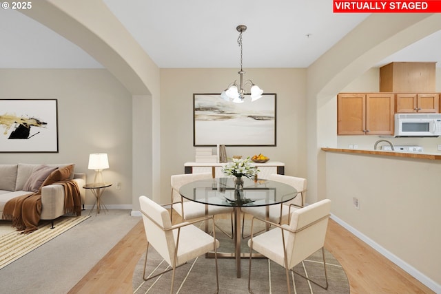 dining space with an inviting chandelier, baseboards, arched walkways, and light wood-type flooring