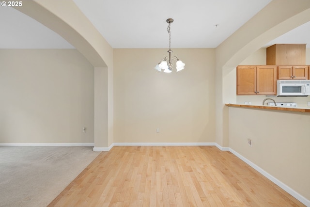 unfurnished dining area featuring baseboards, arched walkways, an inviting chandelier, and light wood-style flooring