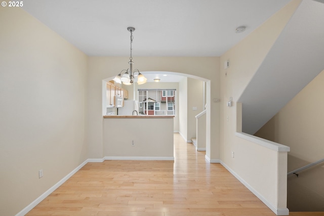 unfurnished dining area featuring light wood finished floors, baseboards, a chandelier, stairs, and arched walkways