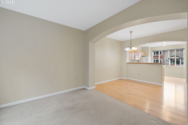 unfurnished room with baseboards, arched walkways, light carpet, light wood-type flooring, and a chandelier