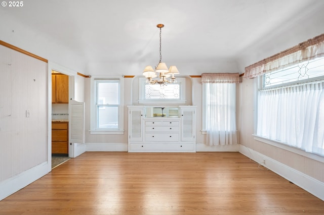 unfurnished dining area with a notable chandelier and light wood-type flooring