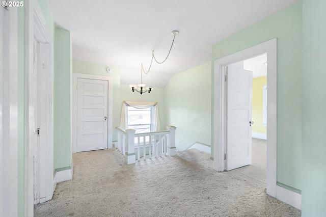 hallway with light colored carpet, lofted ceiling, and a chandelier