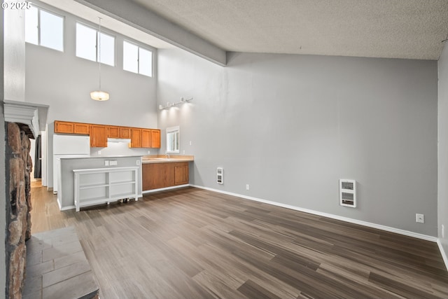 unfurnished living room featuring plenty of natural light, heating unit, a textured ceiling, and hardwood / wood-style floors