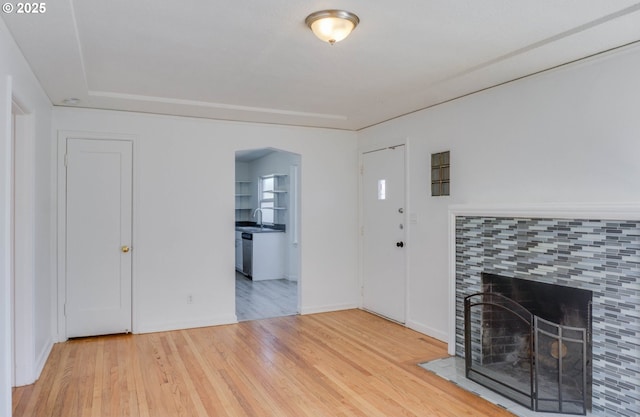 unfurnished living room with a tiled fireplace, wood finished floors, and a sink