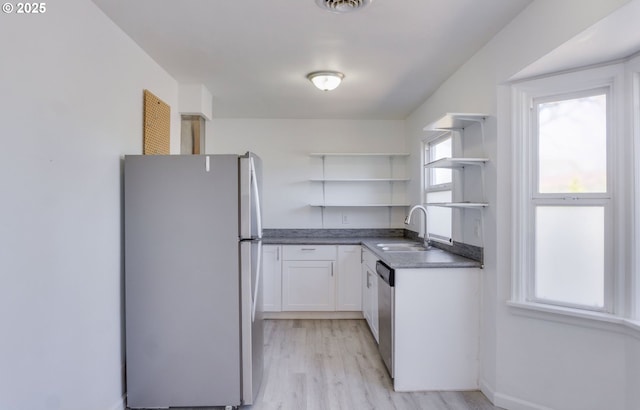 kitchen with open shelves, freestanding refrigerator, white cabinets, a sink, and light wood-style flooring