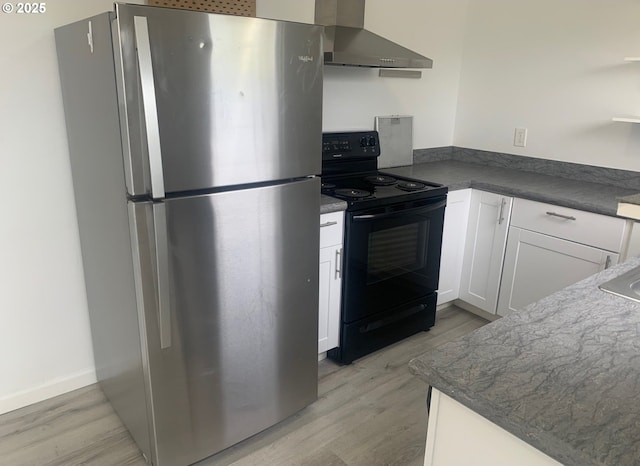kitchen featuring white cabinets, light wood-style flooring, black electric range oven, wall chimney exhaust hood, and freestanding refrigerator