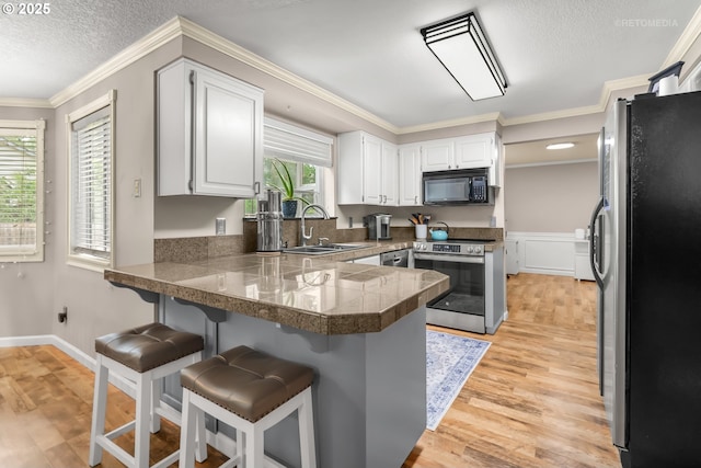 7100 SW 164th Ter, Beaverton, OR 97007 - kitchen with appliances with stainless steel finishes, a sink, a peninsula, light wood-style floors, and a kitchen bar