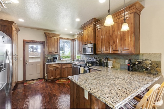 kitchen featuring stainless steel appliances, a peninsula, light stone counters, backsplash, and dark wood-type flooring