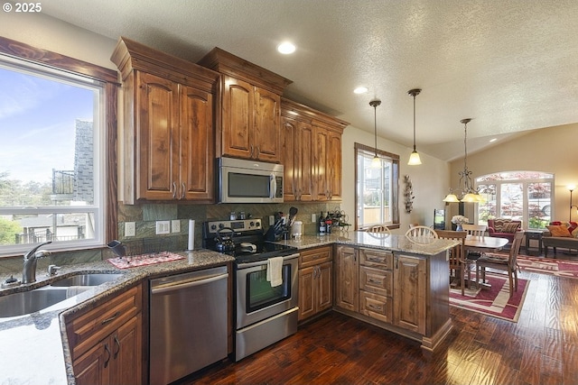 kitchen with appliances with stainless steel finishes, a sink, dark wood-style flooring, tasteful backsplash, and stone countertops