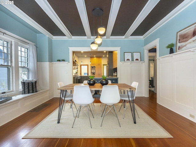 dining room featuring visible vents, dark wood-style flooring, beam ceiling, and a decorative wall