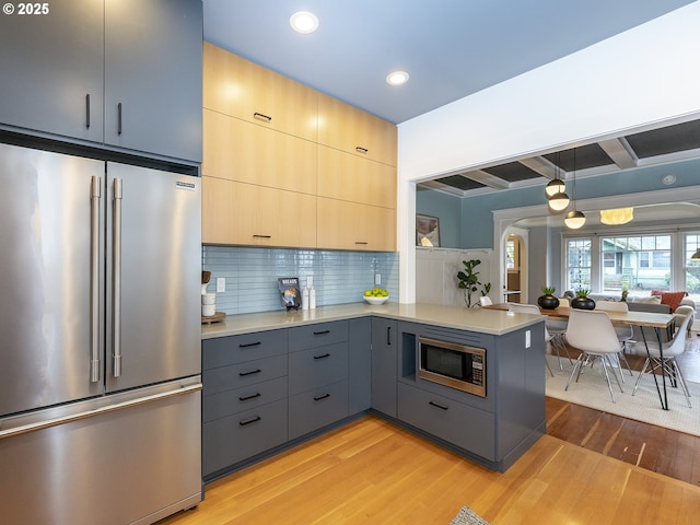 kitchen featuring pendant lighting, stainless steel appliances, light countertops, light brown cabinetry, and a peninsula